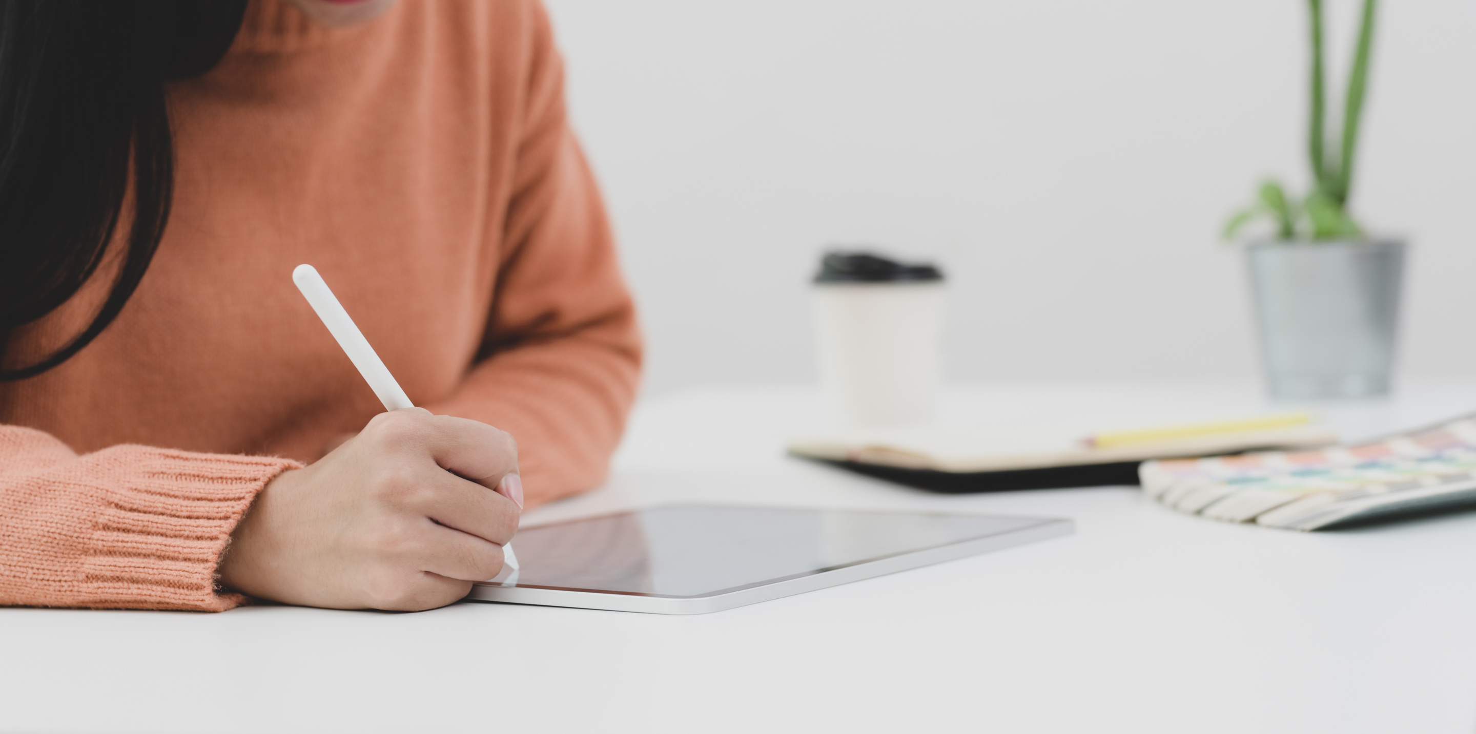 Person in Orange Long Sleeve Sweater Writing on Ipad